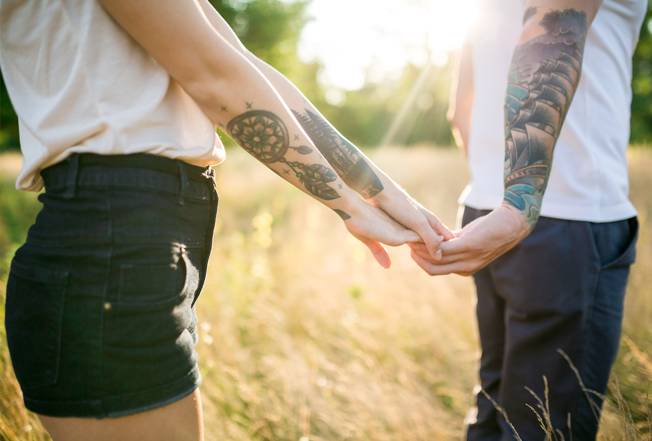 Couple with matching hand tattoos holding hands affectionately.